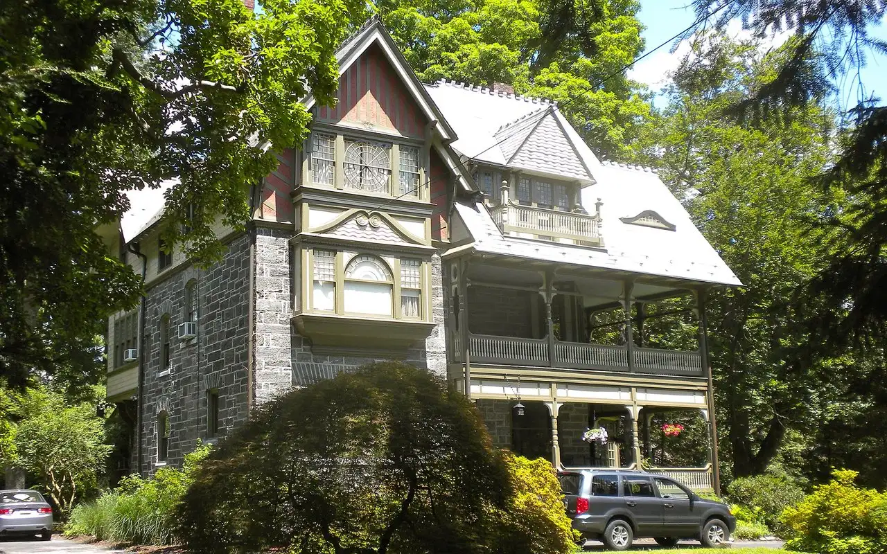 A gray stone Victorian house with a slate roof and wraparound porch in Chestnut Hill