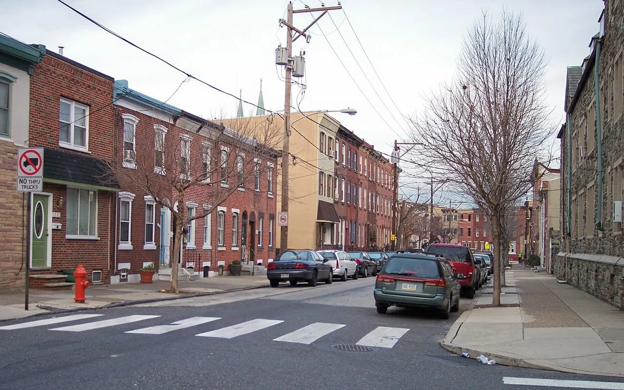 A Fishtown street corner lined with two- and three-story brick rowhouses, with a church spire rising behind them
