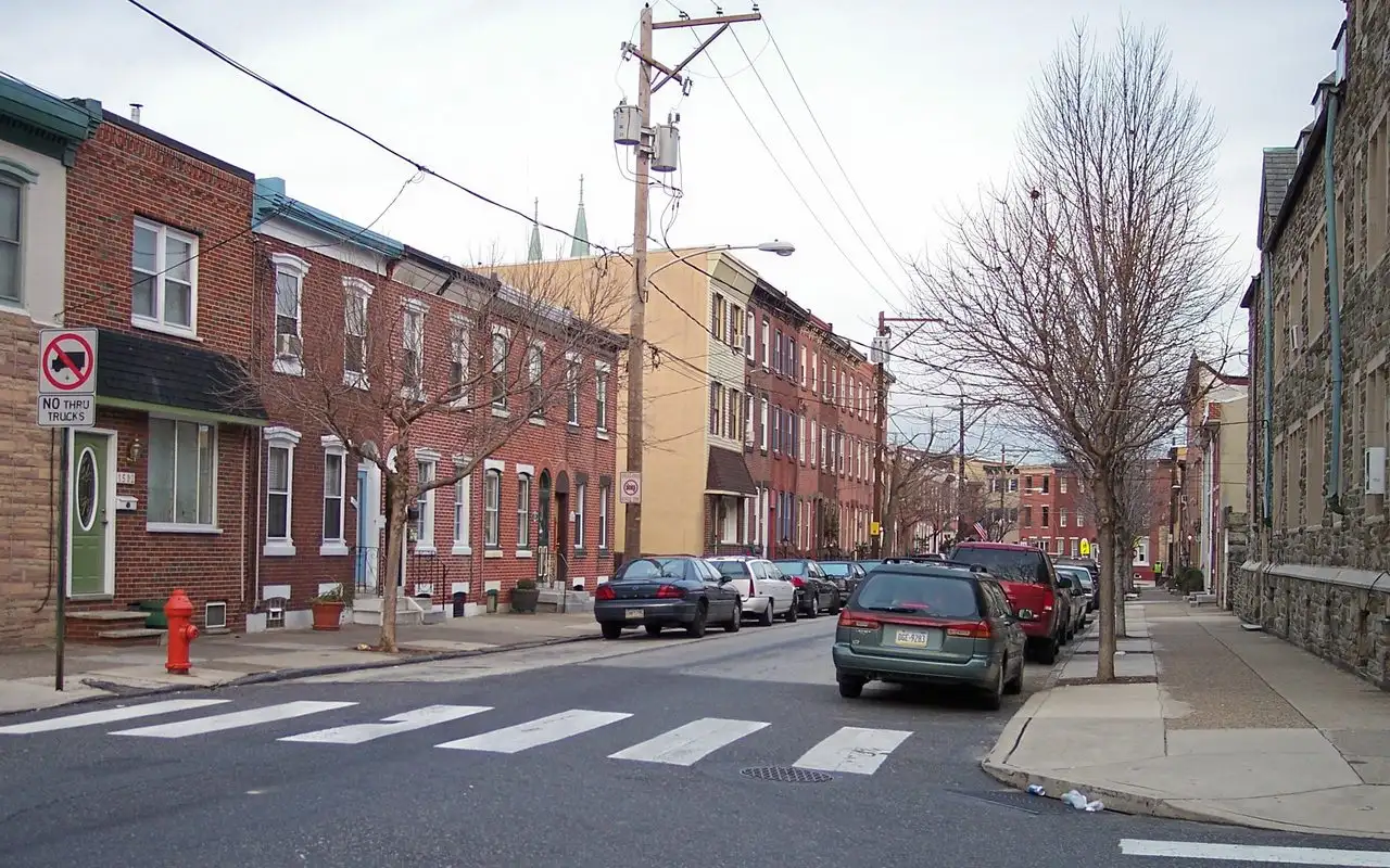 A Fishtown street corner lined with two- and three-story brick rowhouses, with a church spire rising behind them