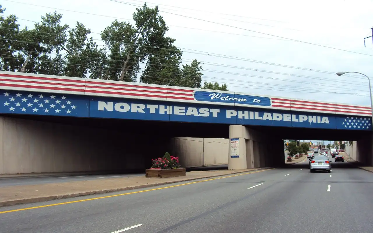 A stars-and-stripes Welcome to Northeast Philadelphia sign painted on an overpass above a wide avenue