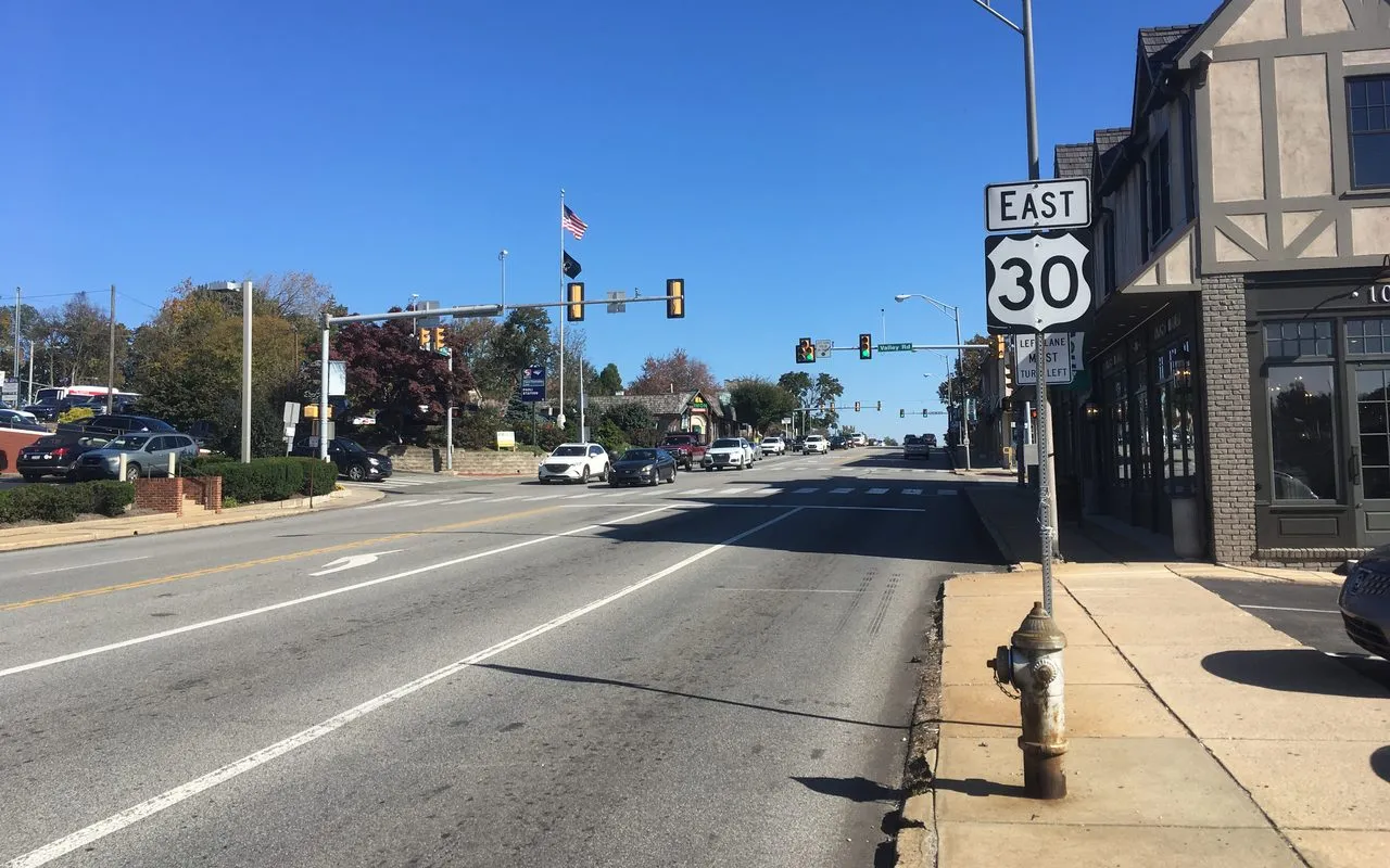 Lancaster Avenue in Paoli on a sunny day, with Tudor-style storefronts on the right and the traffic lights at Valley Road ahead